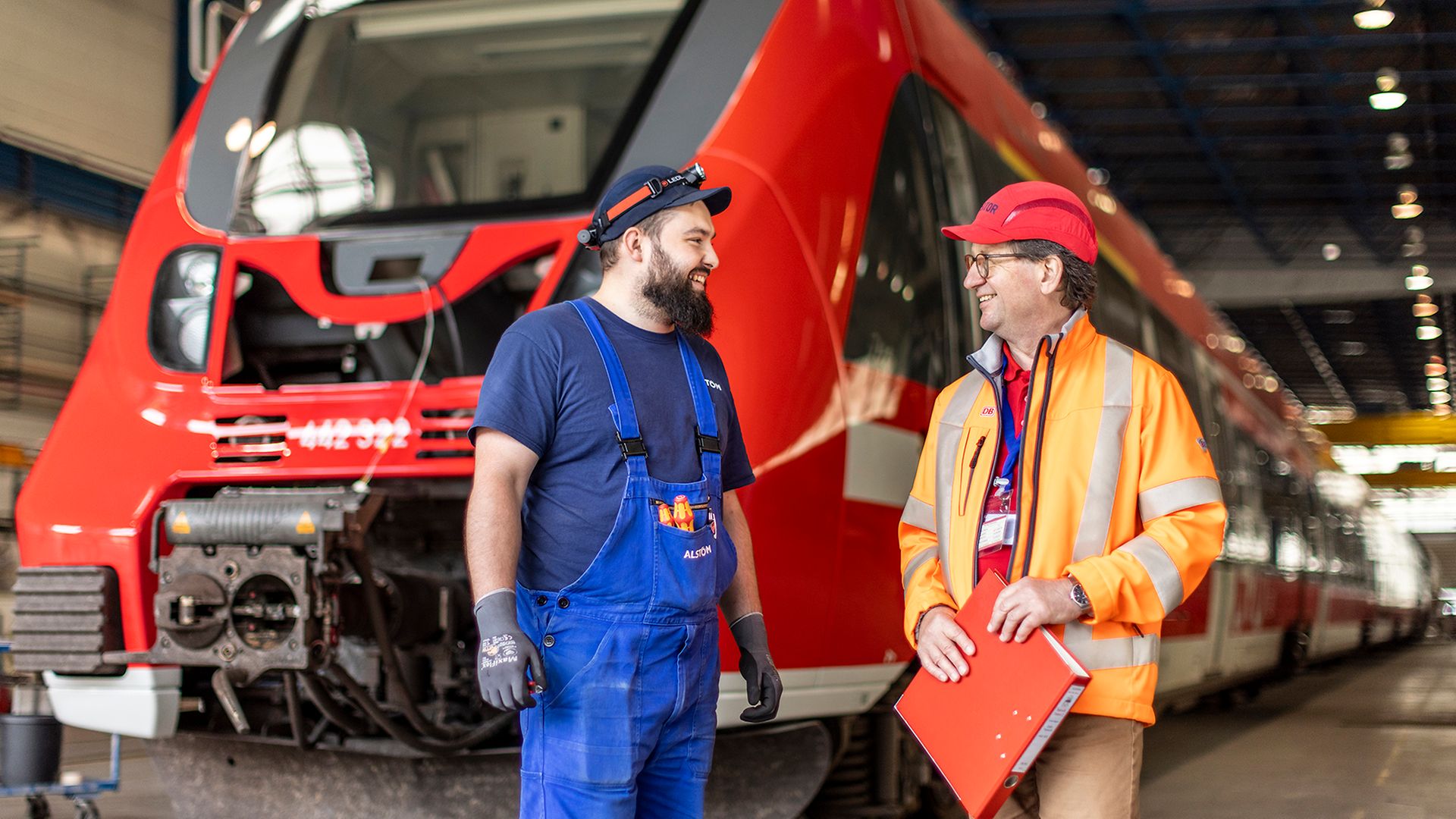 Ein Alstom- und ein DB-Mitarbeiter stehen in der Werkshalle vor einem Zug und tauschen sich aus