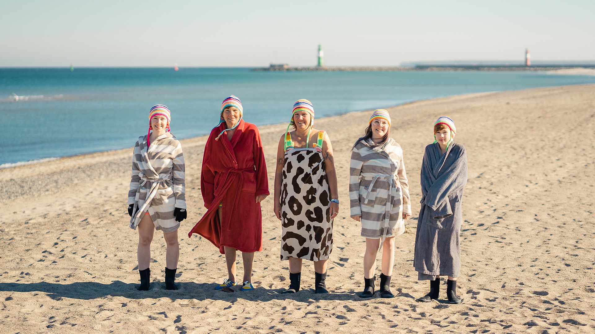 Vier Frauen unterschiedlichen Alters stehen in bunten Bademänteln am Strand in Warnemünde.