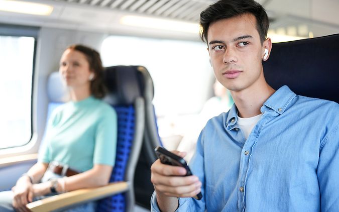 Zwei junge Erwachsene sitzen im Regionalzug, einer hat ein Smartphone in der Hand.