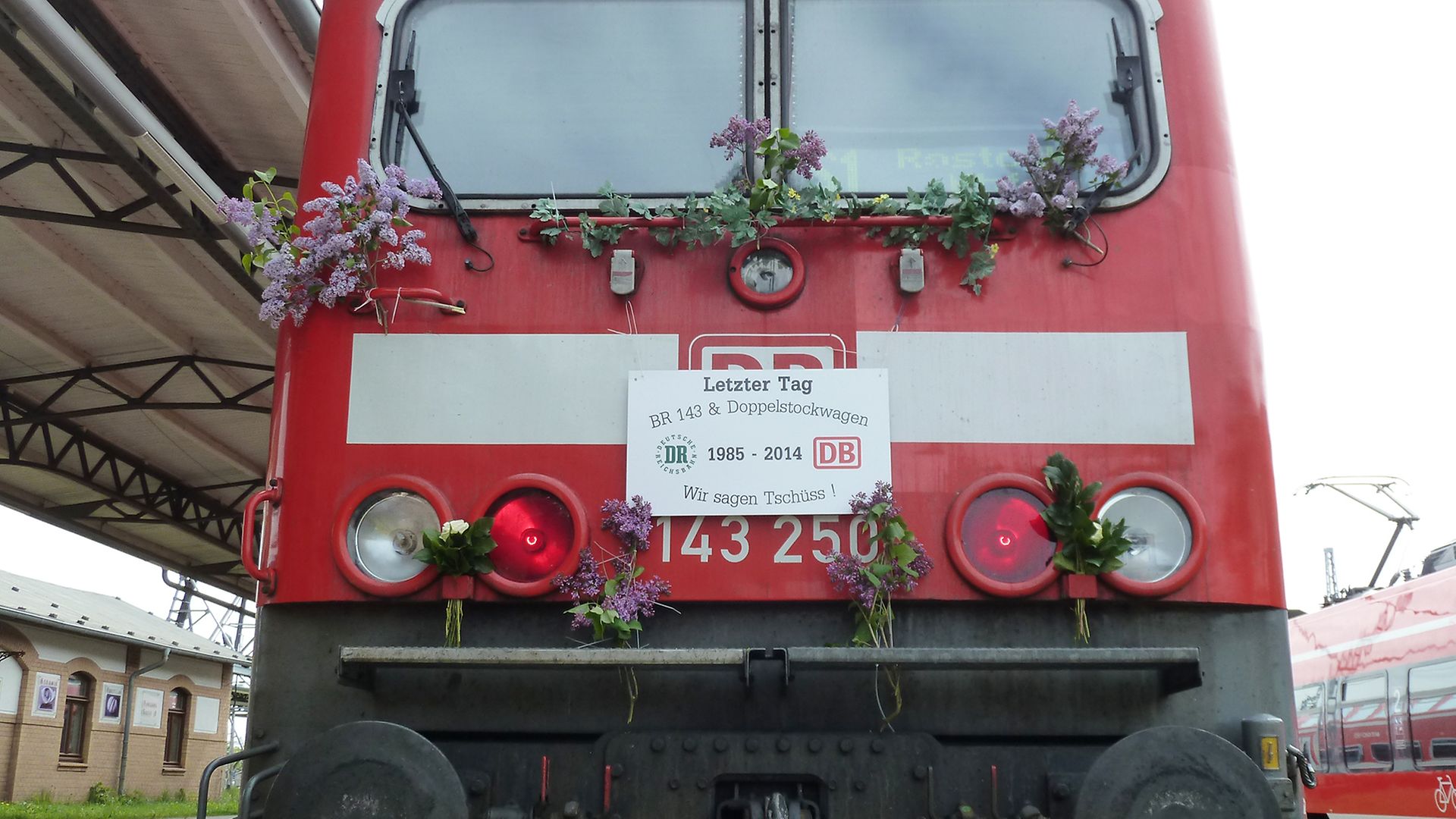 Auf einem Triebwagen ist ein Schild angebracht: "Letzter Tag BR 143 & Doppelstockwagen 1985 bis 2014. Wir sagen Tschüss!"