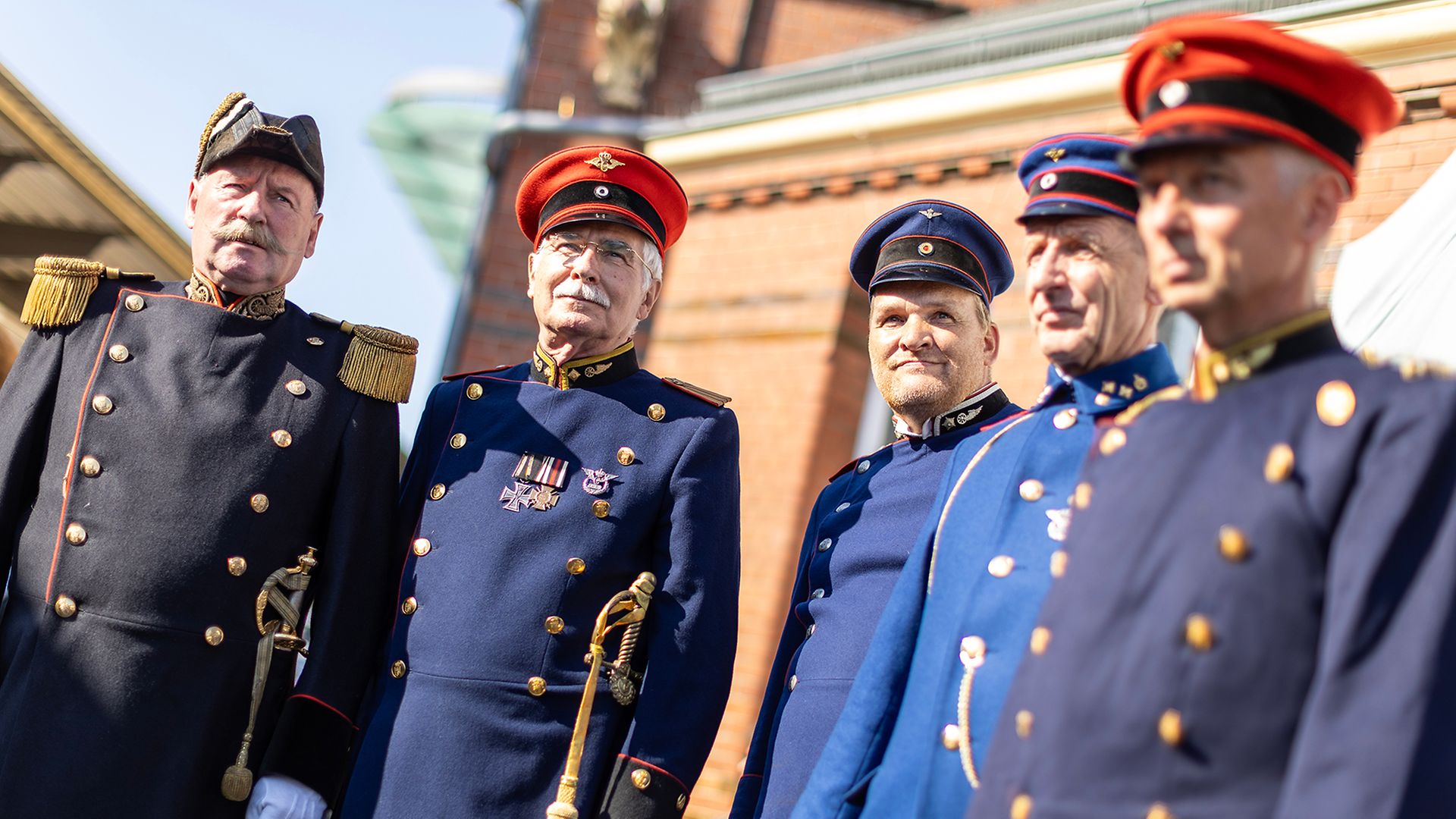 Fünf Herrn präsentieren während einer Modenschau historische Bahnuniformen