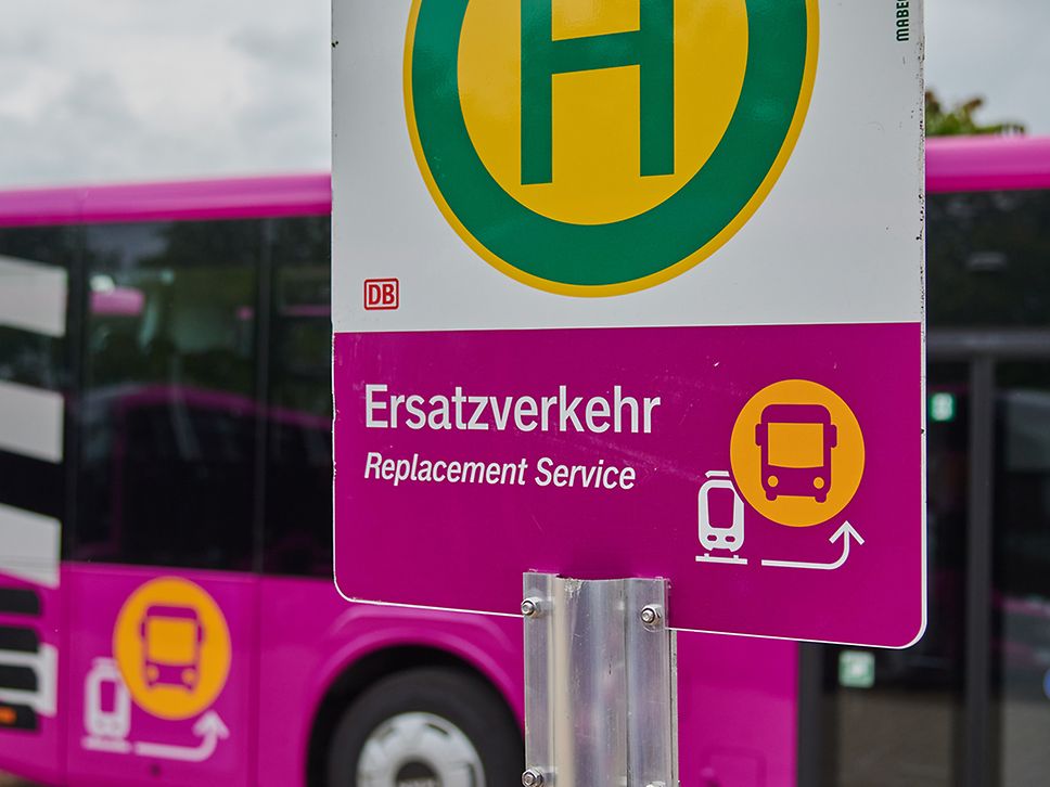 Schild „Ersatzverkehr“ vor purpurnem Bus des Schienenersatzverkehrs 