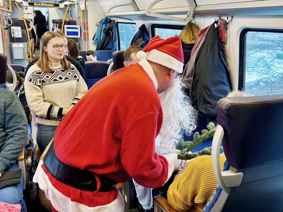 Ein verkleideter Weihnachtsmann im Regionalzug reicht einem Fahrgast seine Geschenke 